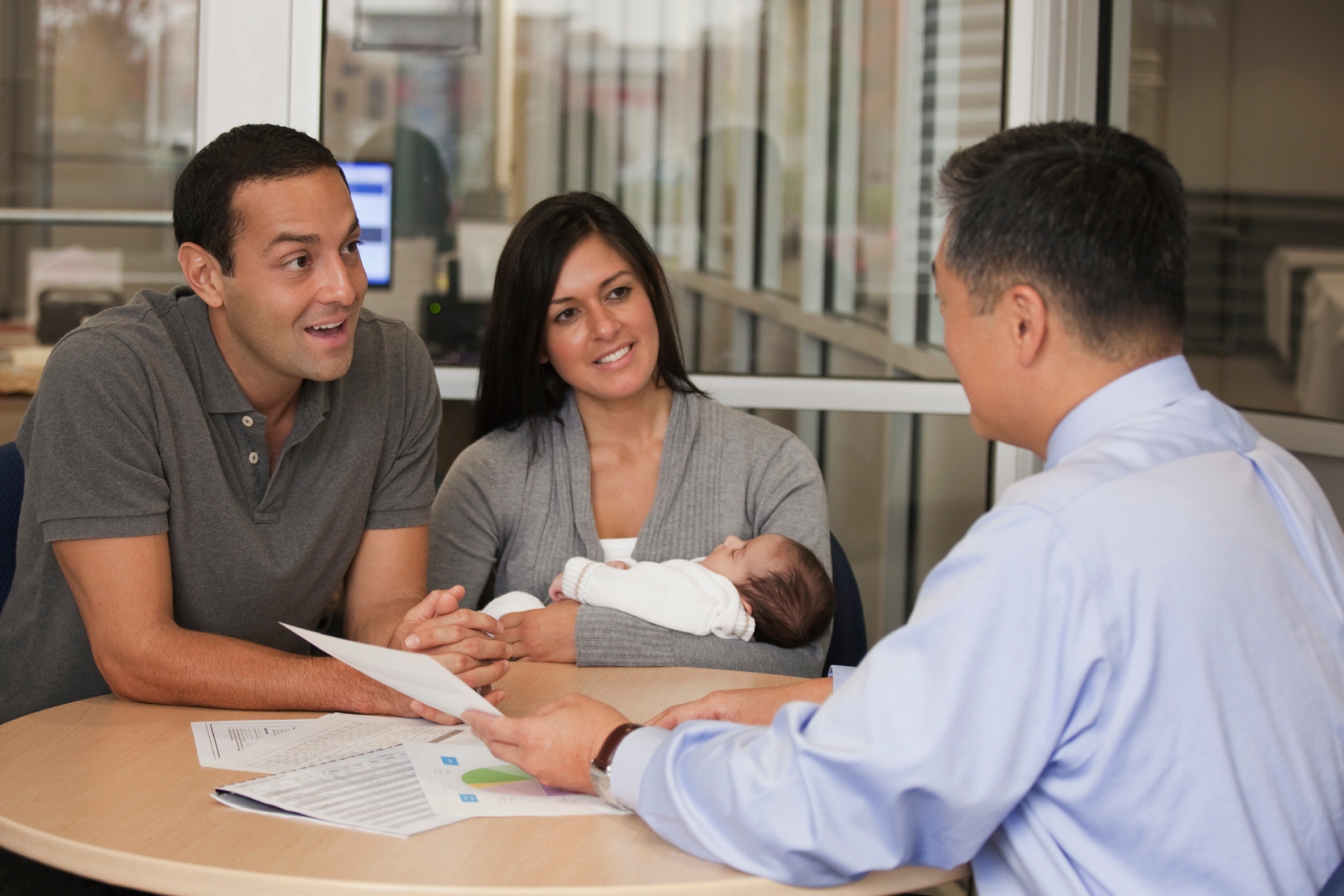 A couple sitting with their young baby at a desk having a meeting with a financial adviser.