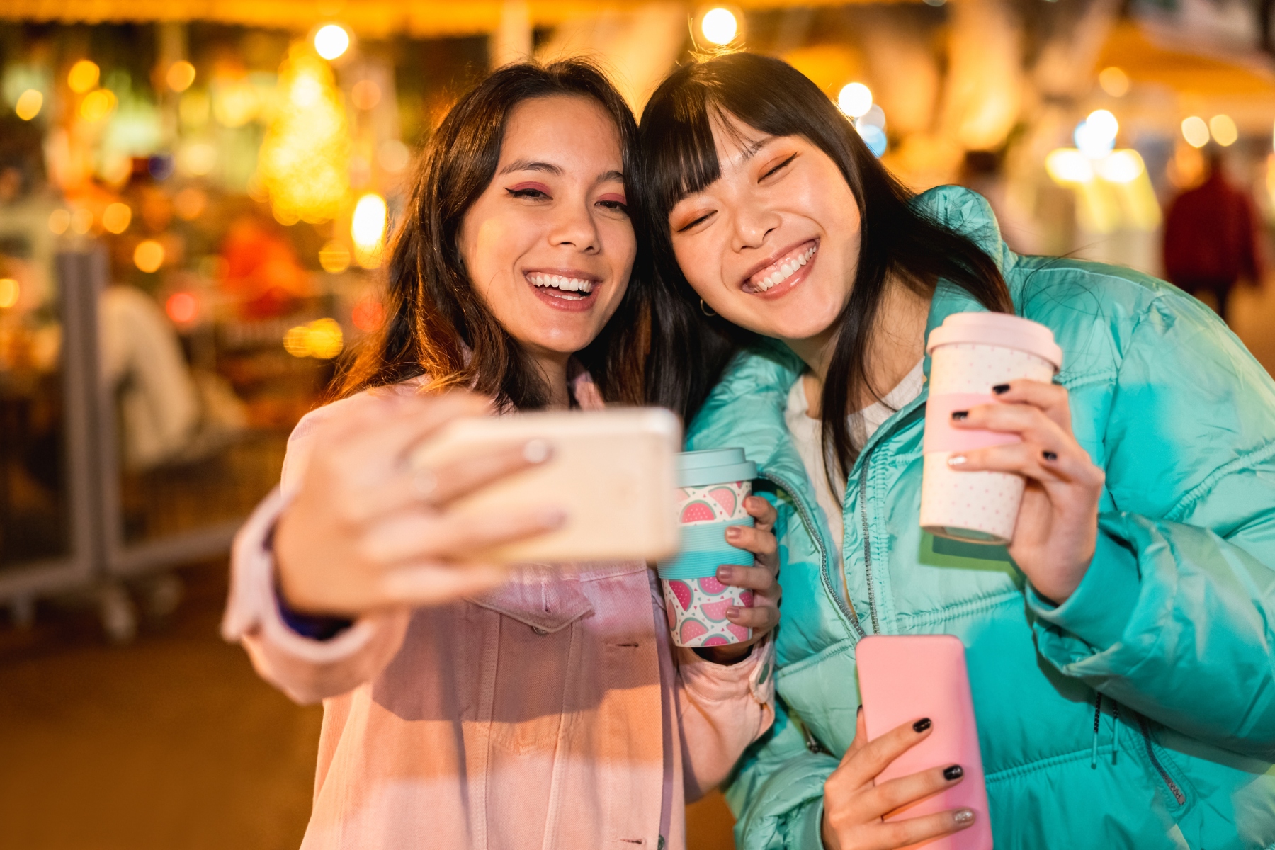Two young women taking a selfie while holding reusable coffee cups
