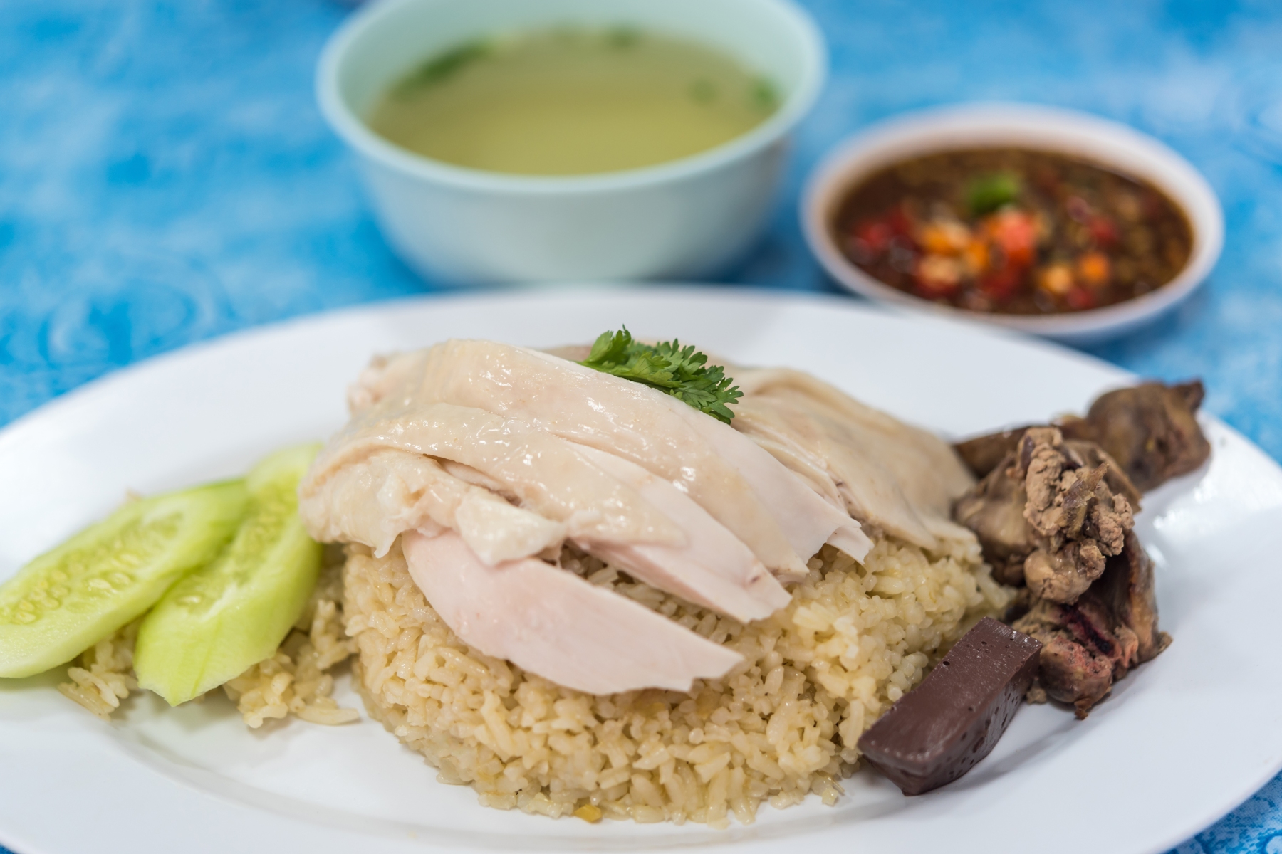 Steamed Hainese chicken rice served with cucumber, liver, soup, and sauce