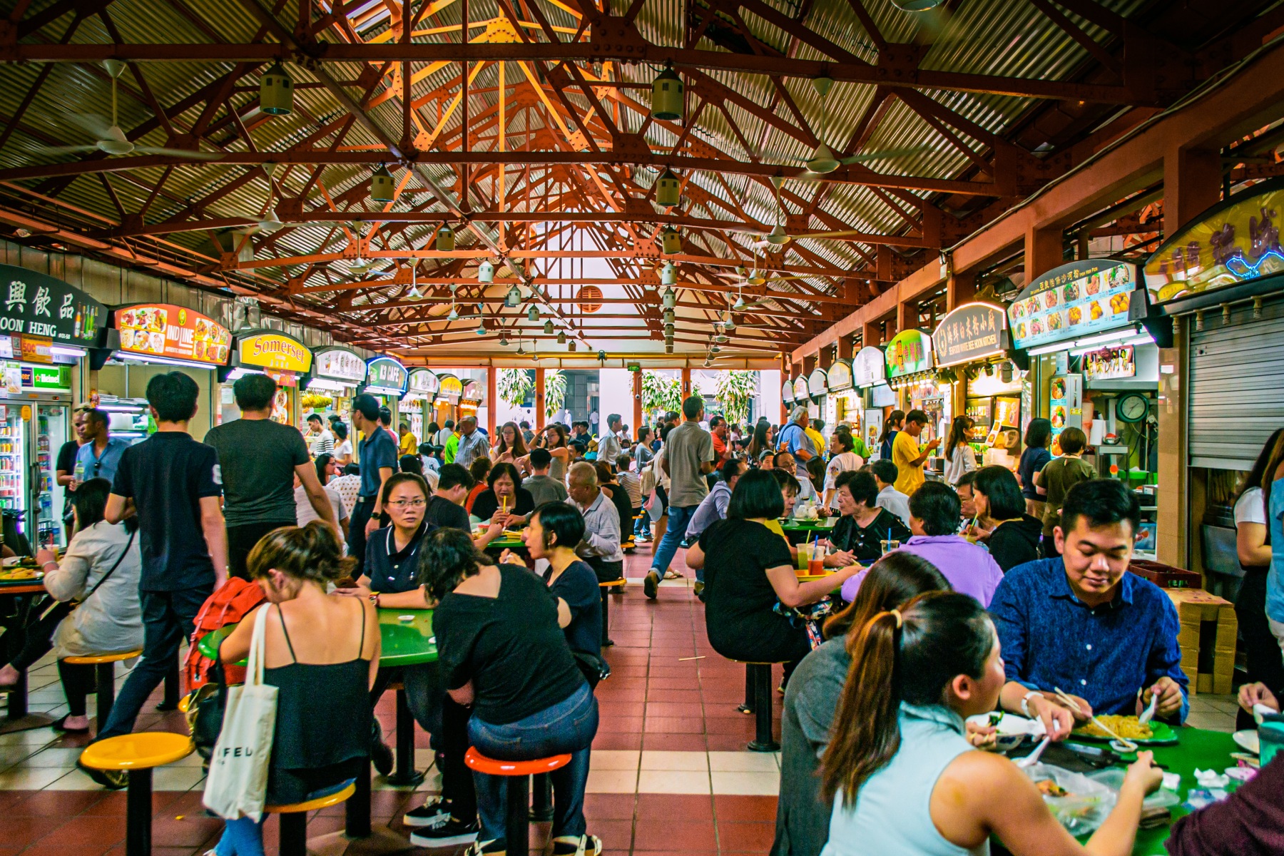 Busy hawker center with food stalls and customers, enjoying Singaporean cuisine