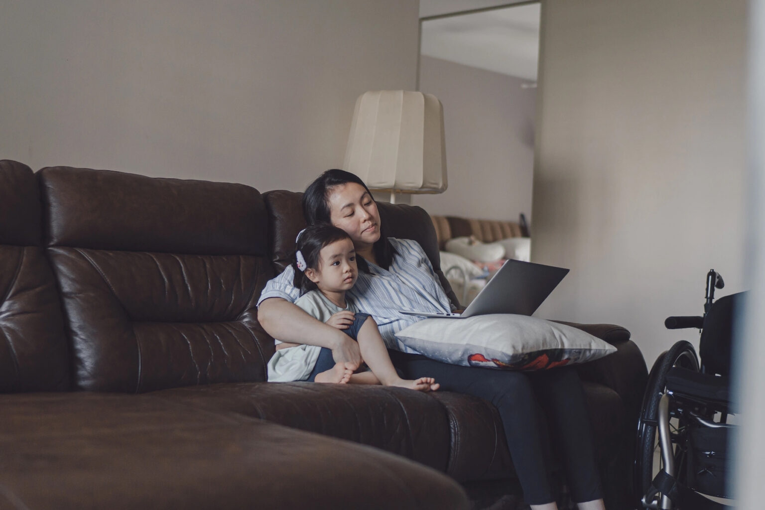 A mother and young daughter sit together on the couch watching a video on a laptop