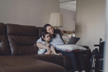 A mother and young daughter sit together on the couch watching a video on a laptop