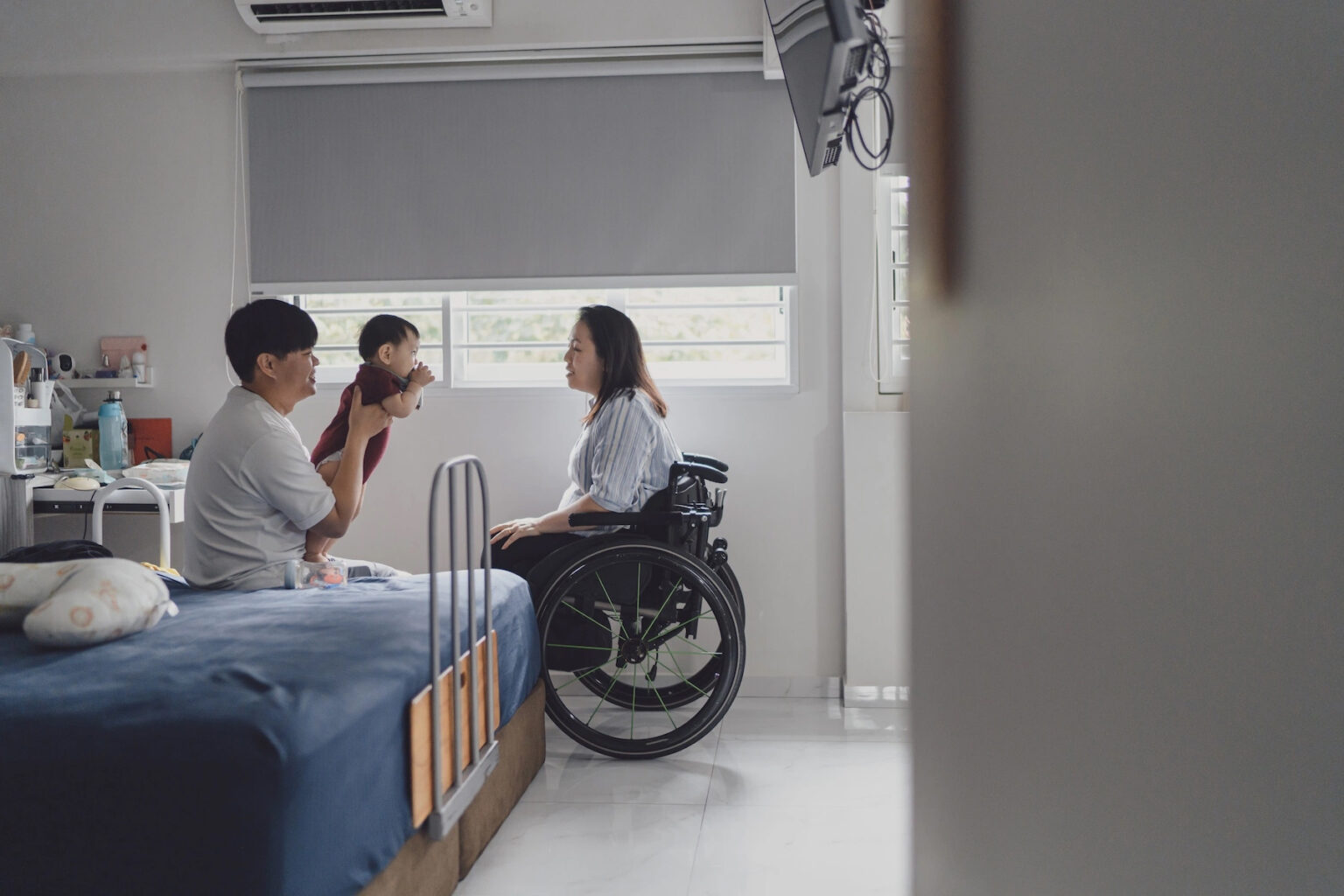 A young family spends time together in a sunny hospital room, the mother is in a wheelchair
