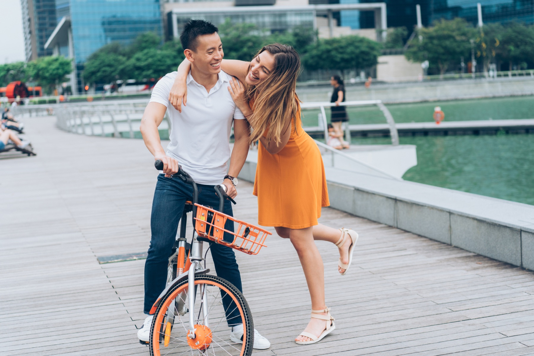 An man on a bicycle laughing with his girlfriend as she put her arm around him. They're standing in Marina Bay.