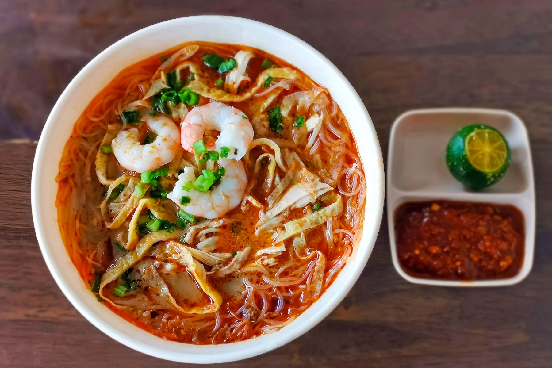 Laksa with noodles, prawns, and chicken in a spicy broth with a side of lime and sambal