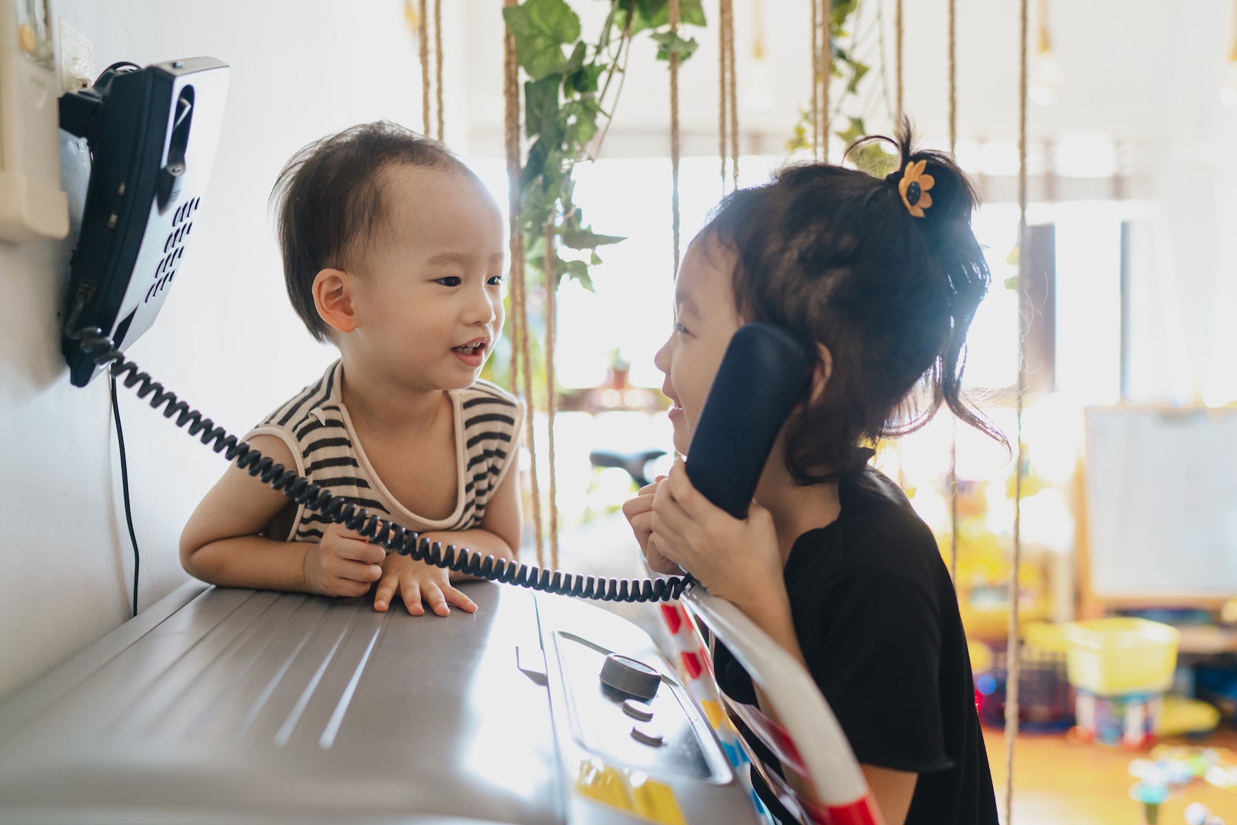 Two small children play and laugh while pretending to talk on a landline phone