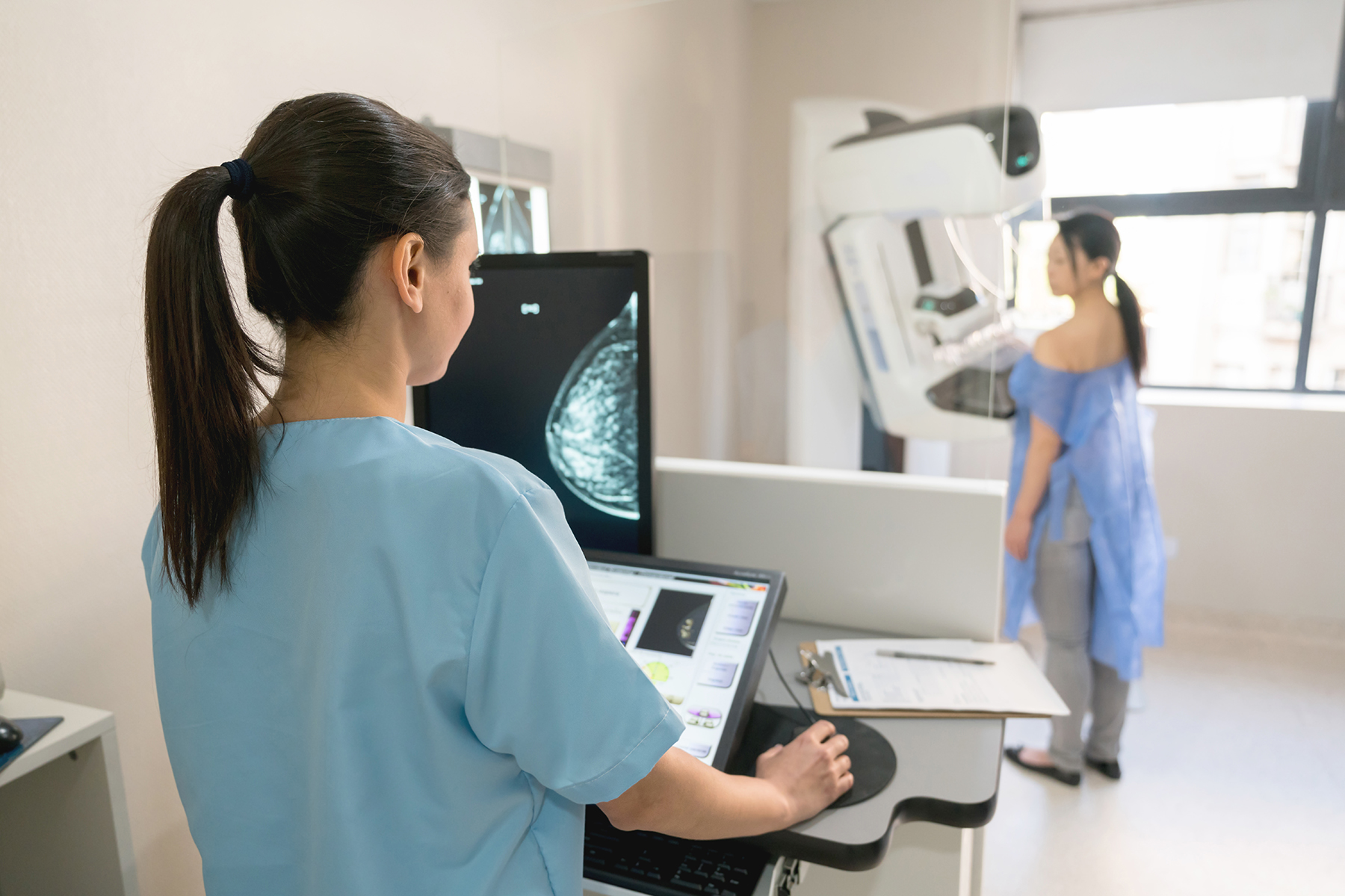 Nurse looking at the images from the patient's mammogram as she is doing the exam

