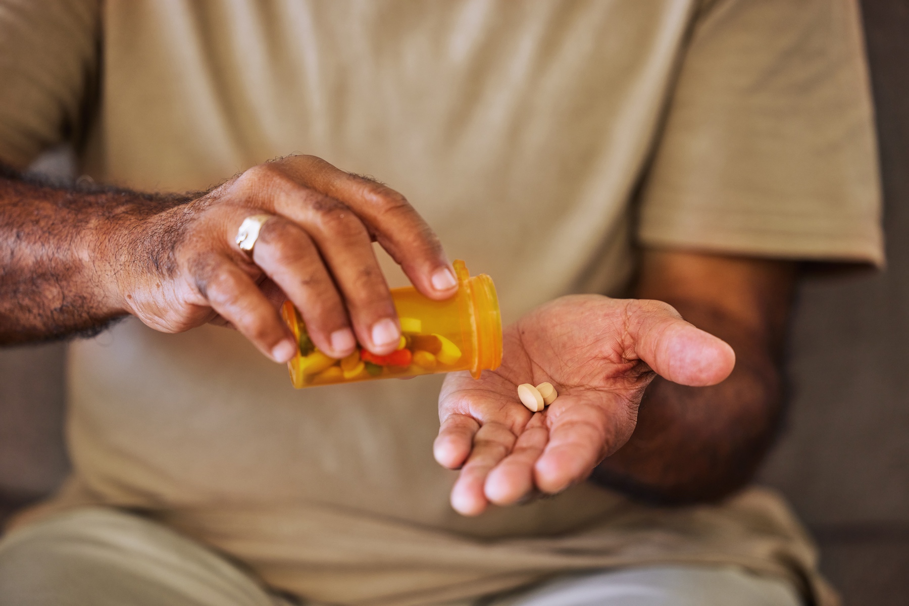 A close-up of pills in the hands of an older adult man as he takes his daily medication

