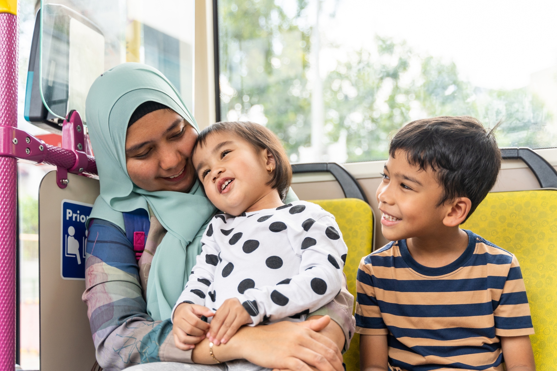 Smiling mother with two young children sit on bus together on the way to school