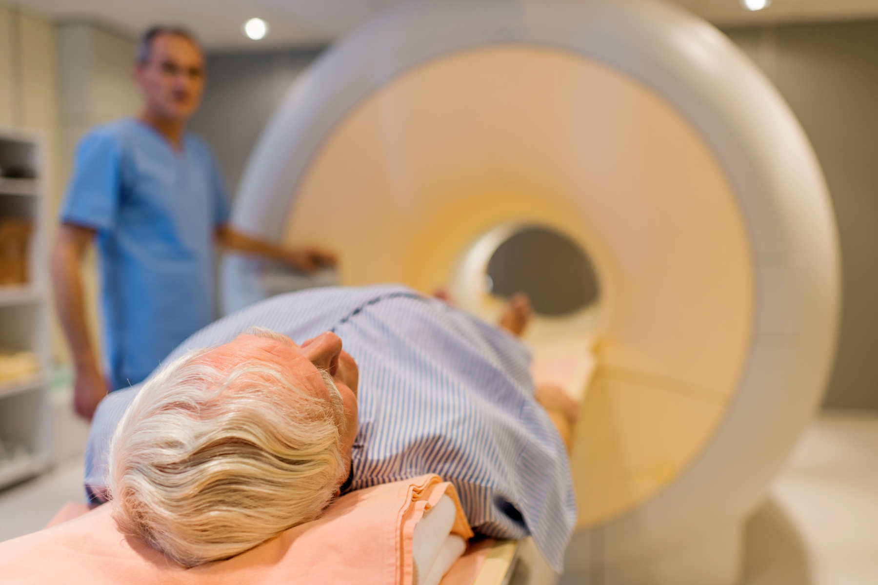 Senior patient laying down to receive an MRI scan with a radiologist standing nearby 
