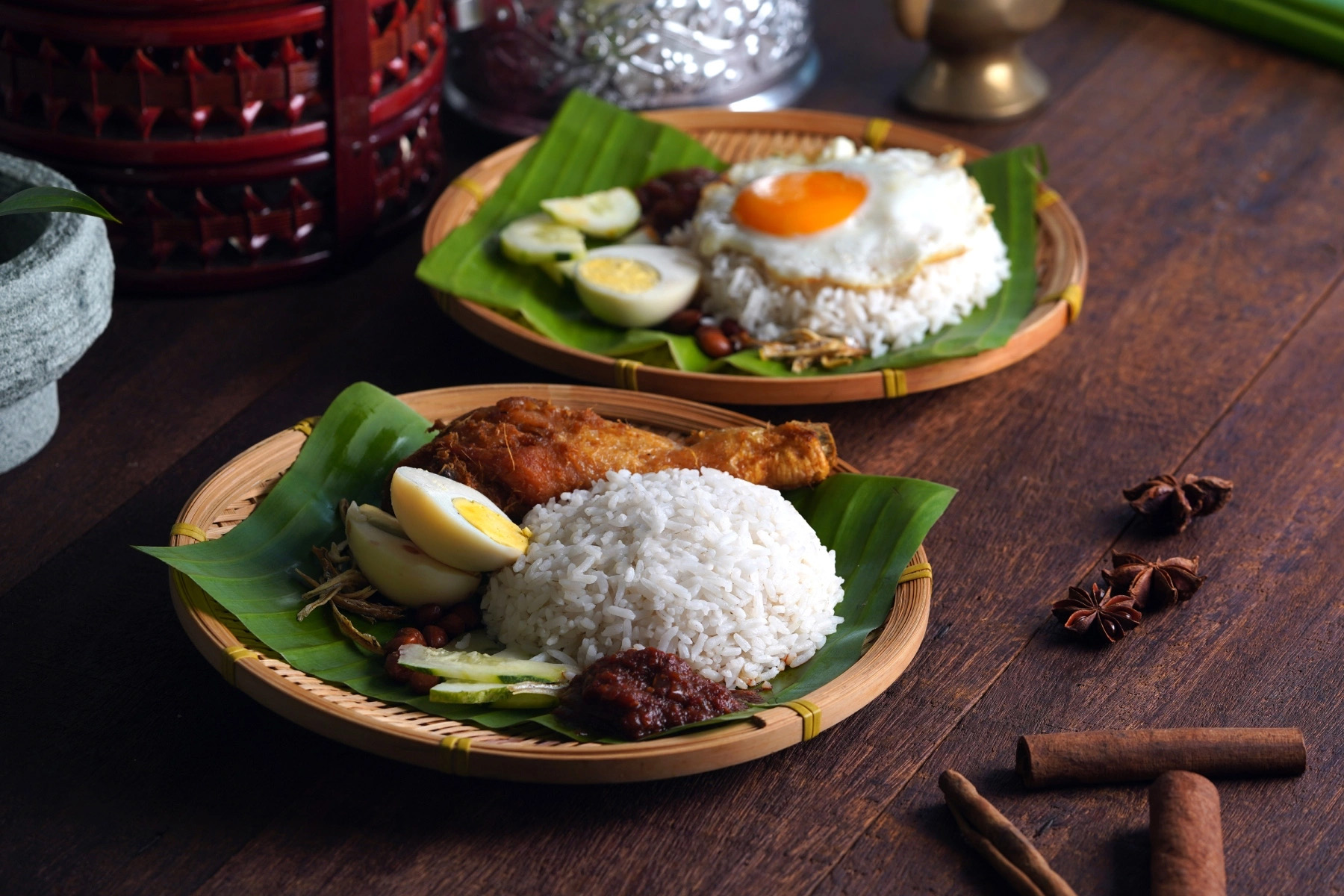Two dishes of nasi lemak served on banana leaves. One is topped with an egg and the other isn't