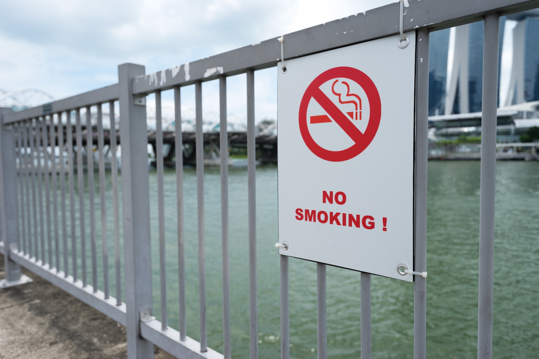A white sign reads 'no smoking' on a steel railing by river

