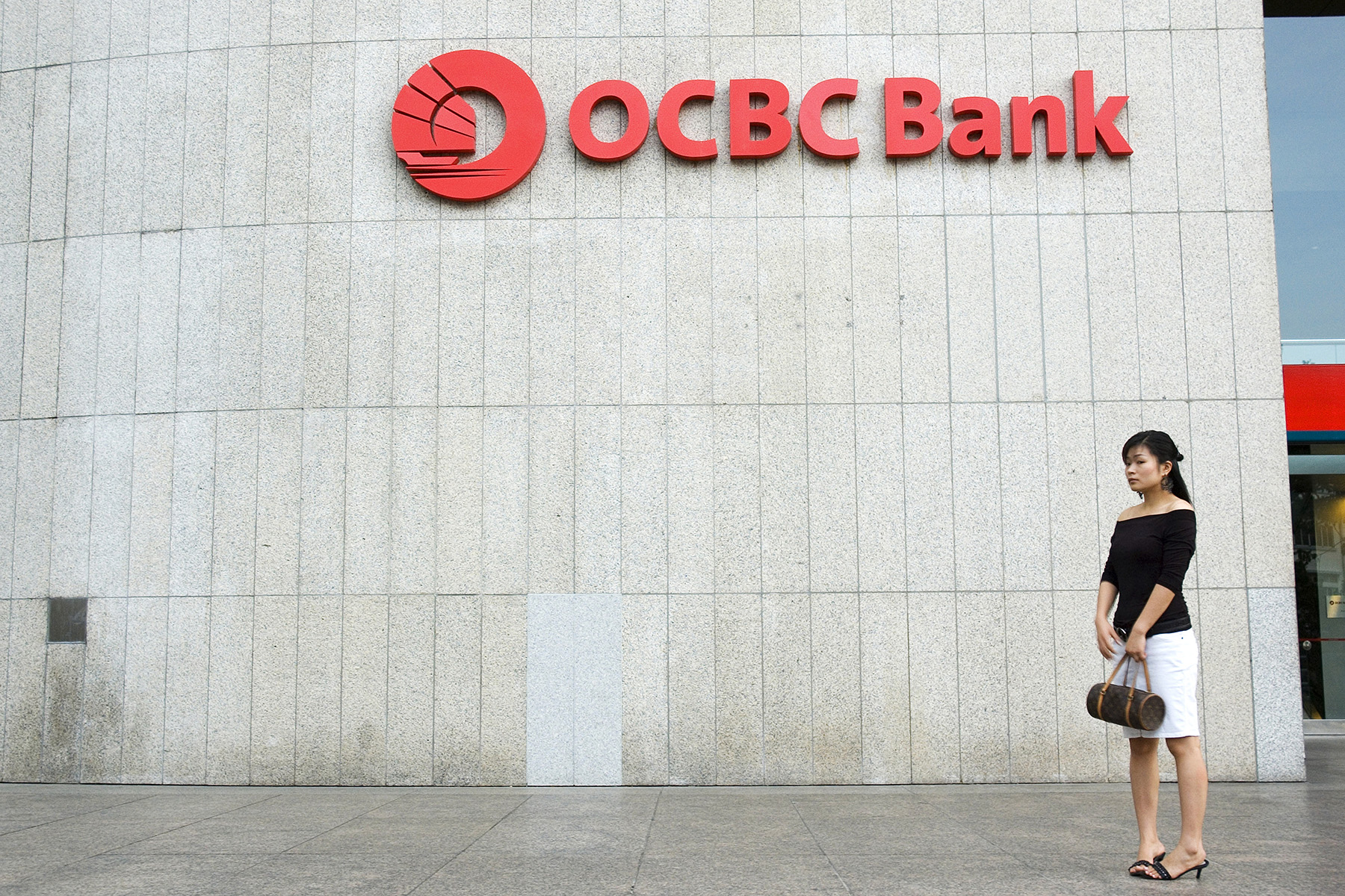 A woman stands in front of the OCBC Bank building in the Raffles Place banking district in Singapore

