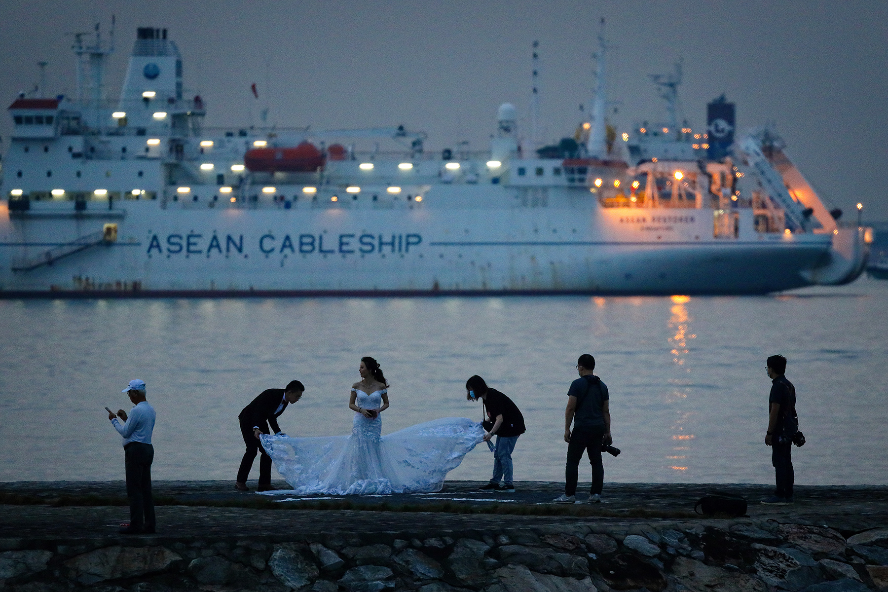 A couple prepare for a photoshoot in front of a ship in the water