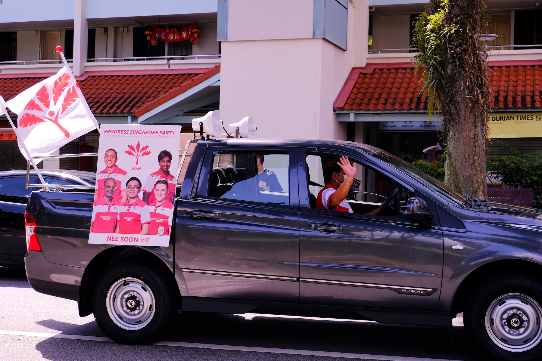 A Progress Party Singapore vehicle  drives down the street as the driver waves to people during the 2020 campaign