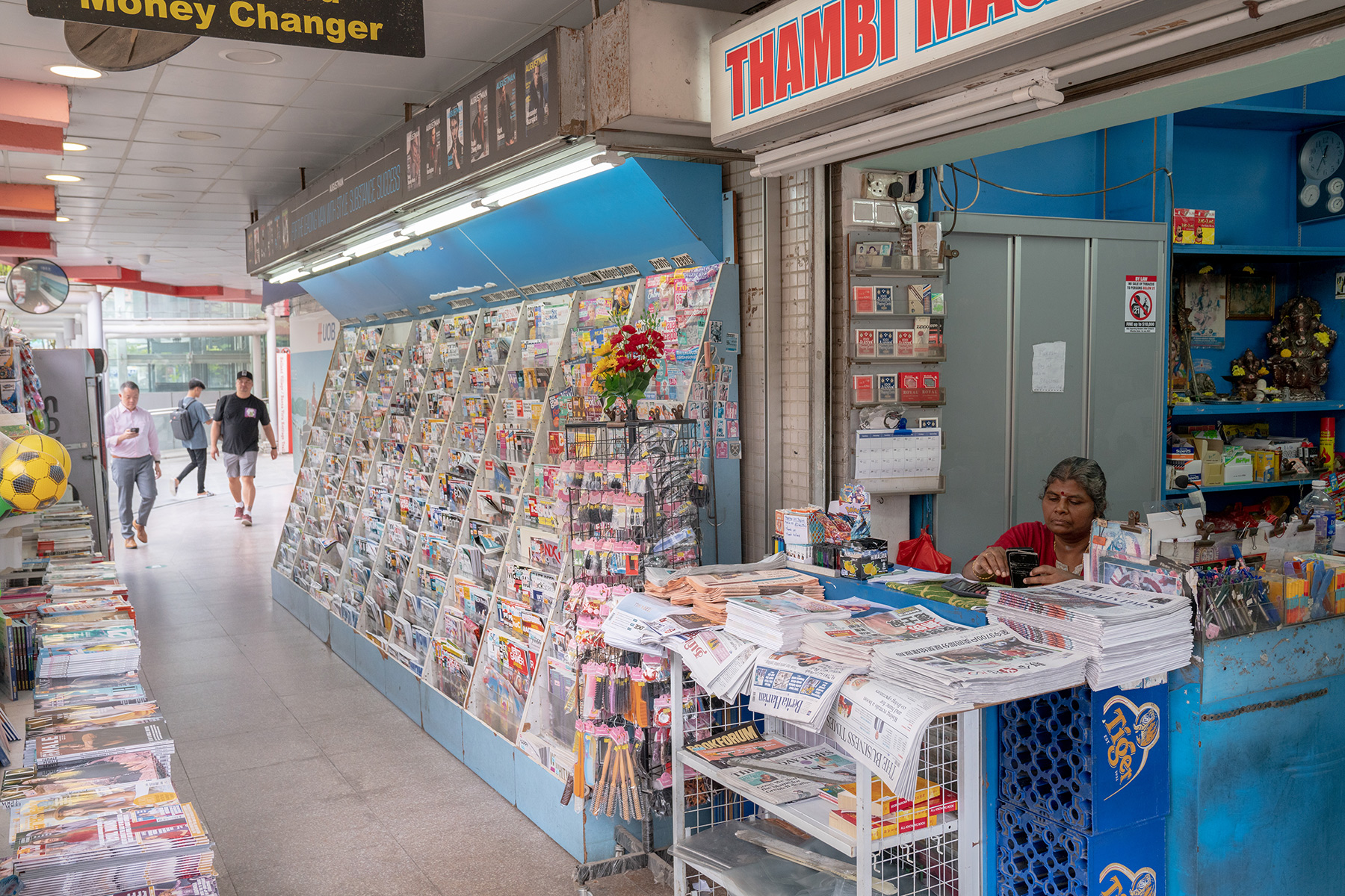 A woman selling magazines and newspapers at a newsagent.