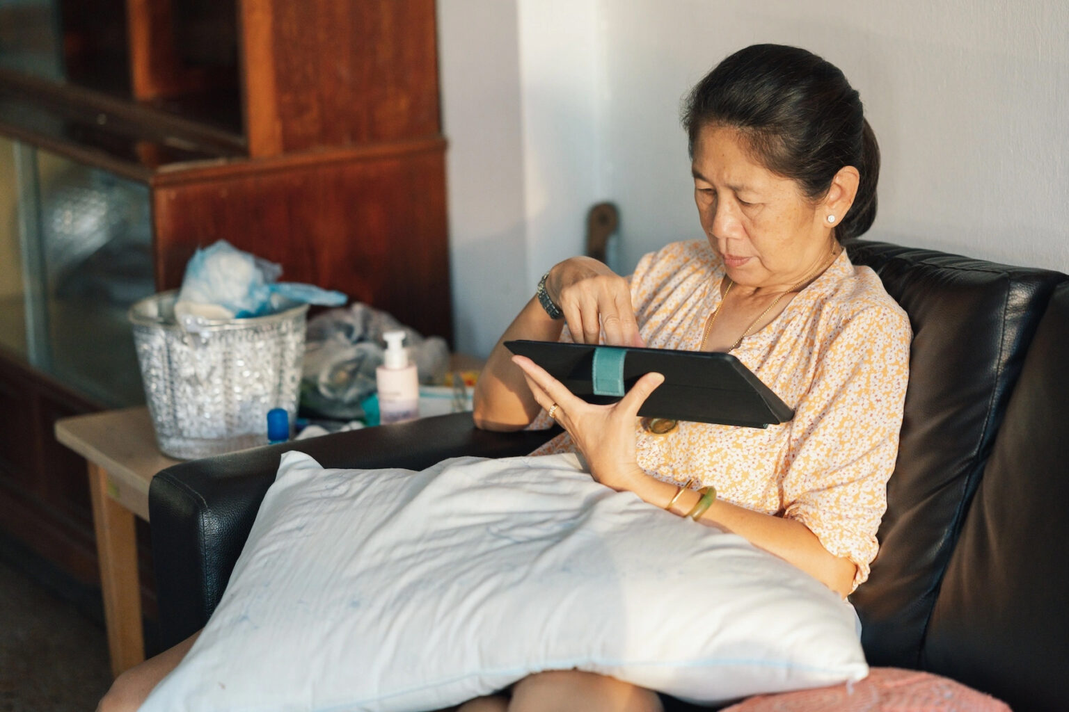 An older woman sits comfortably at home while using an app on her tablet
