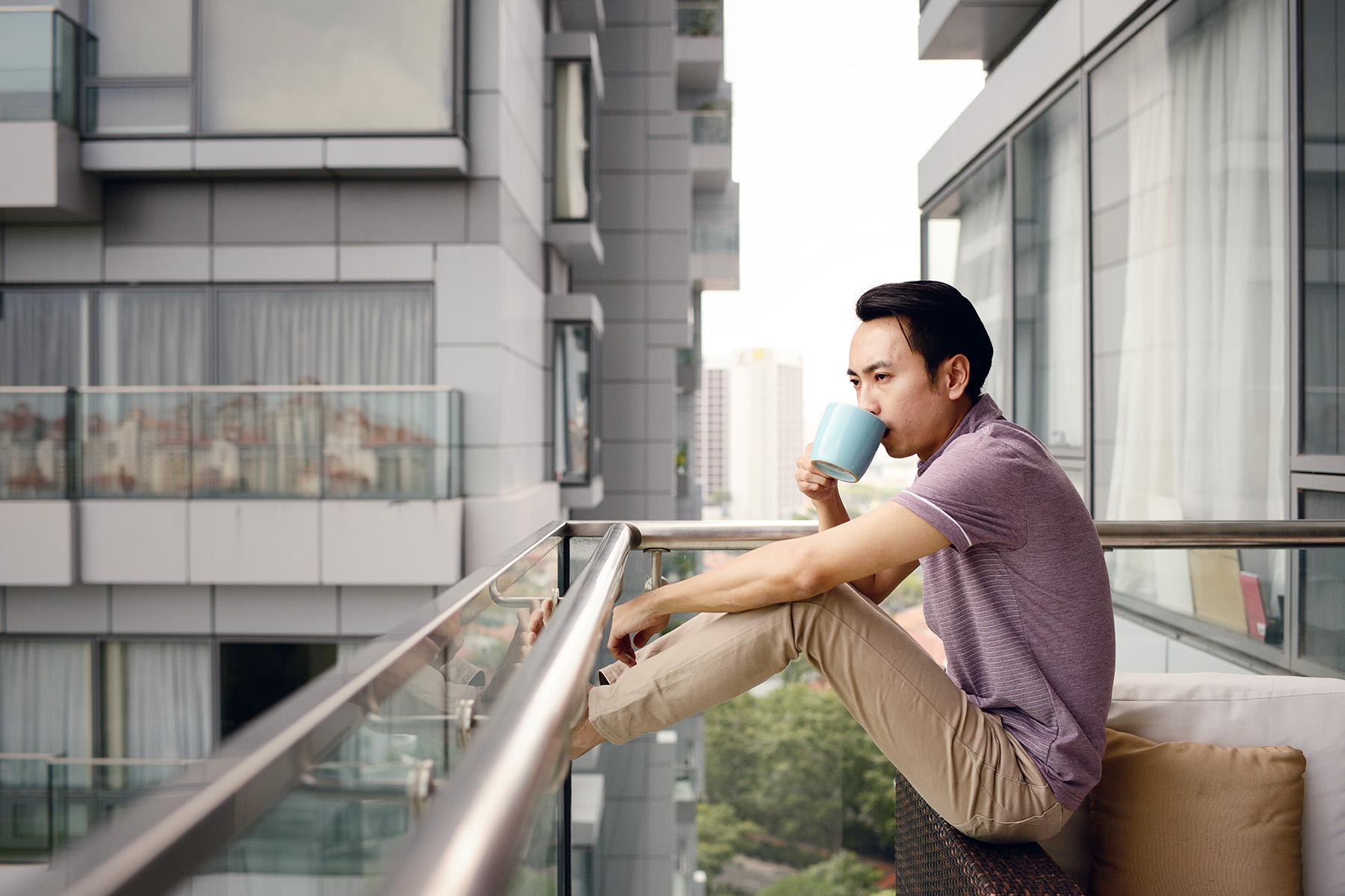 Man sitting on his balcony, drinking coffee. He has his feet on the side pannel.