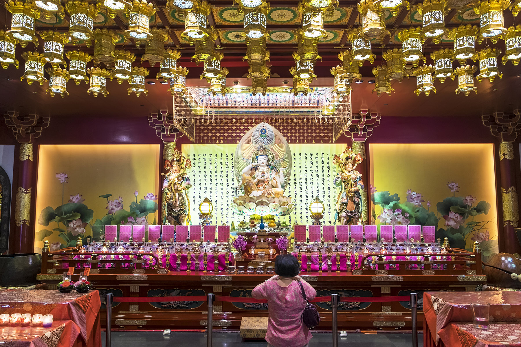 Woman worshipping in front of a brightly adorned altar at Buddha Tooth Relic Temple in Singapore.