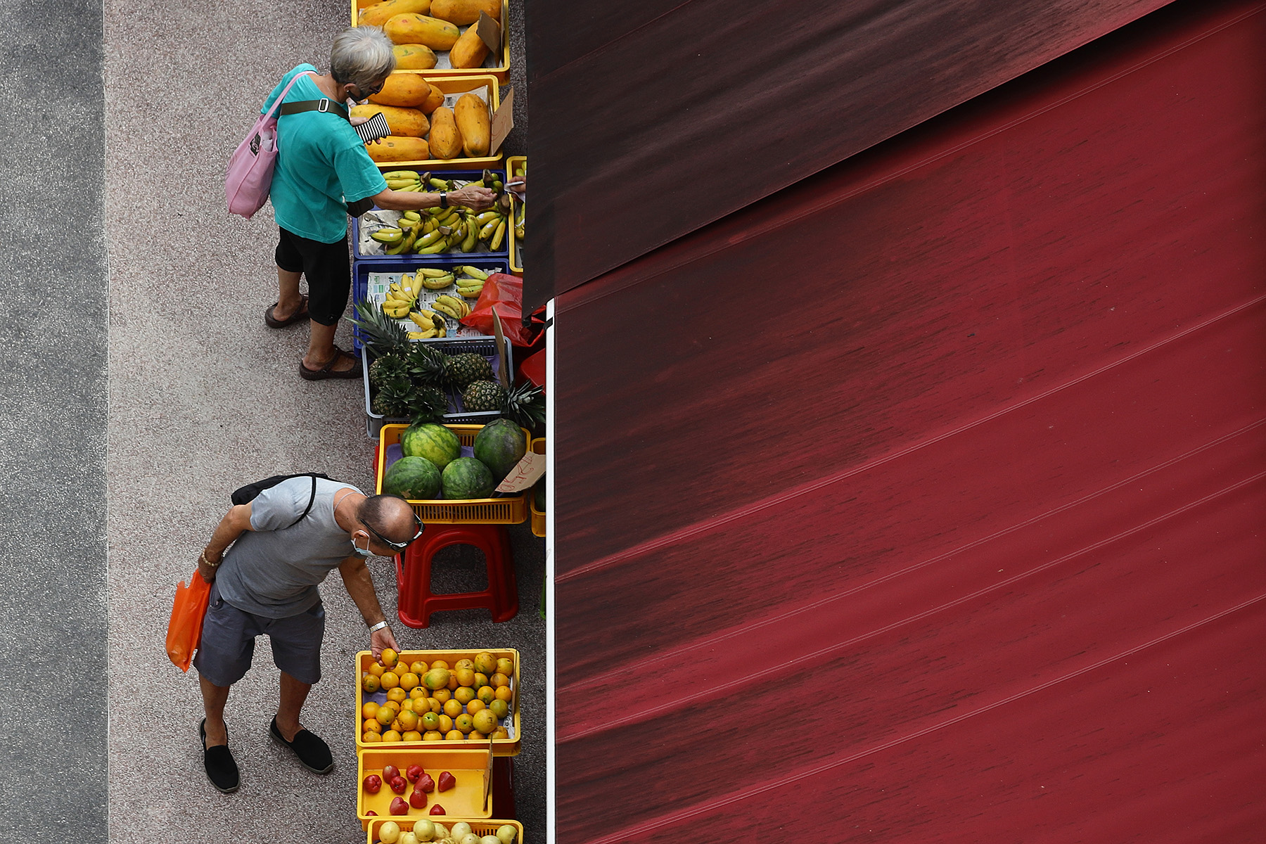 Aerial view of people wearing protective mask shop for fruit under a dirty sunblind in Singapore.