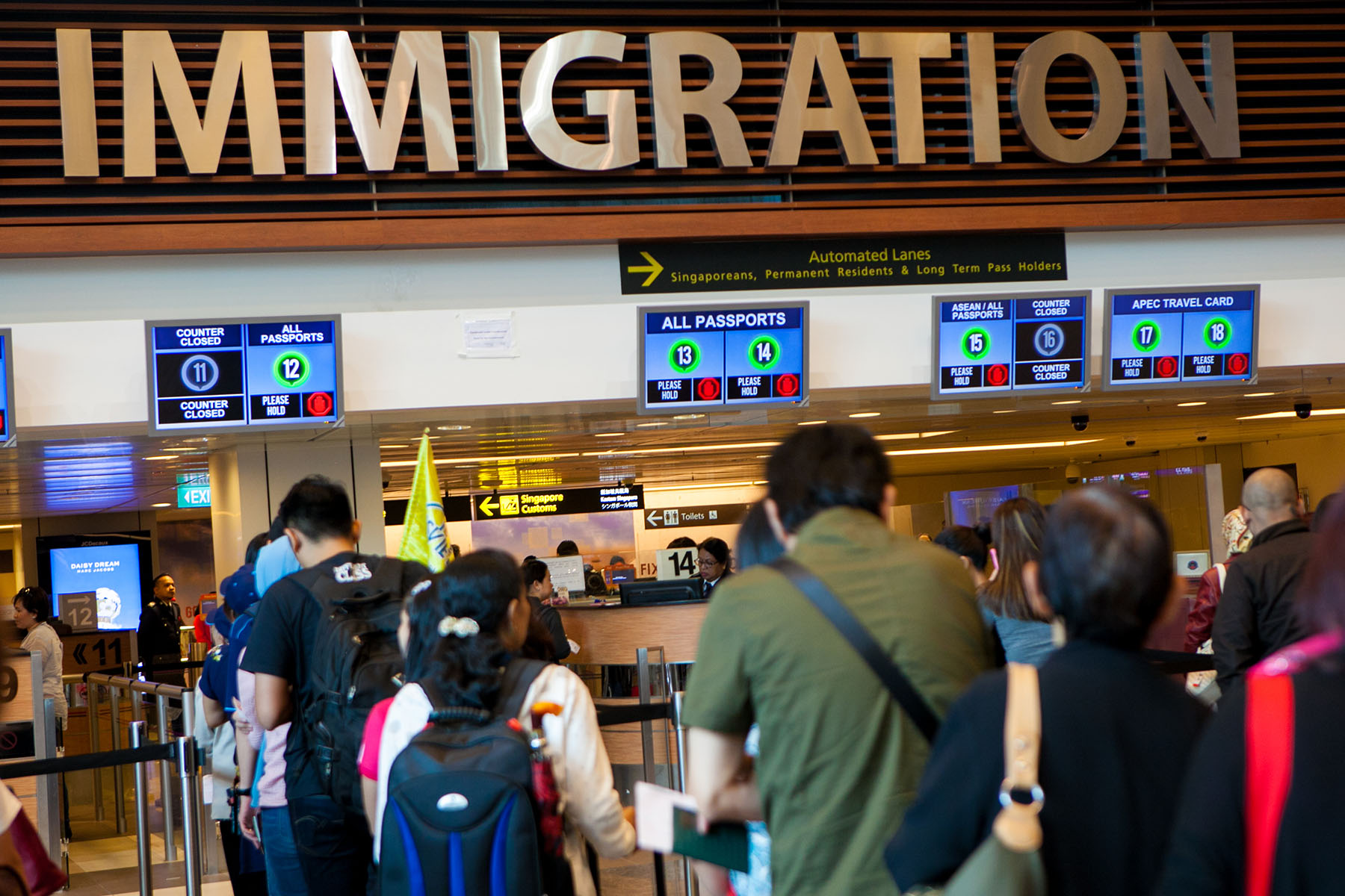 People standing in line in front of an airport immigration desk in Singapore.