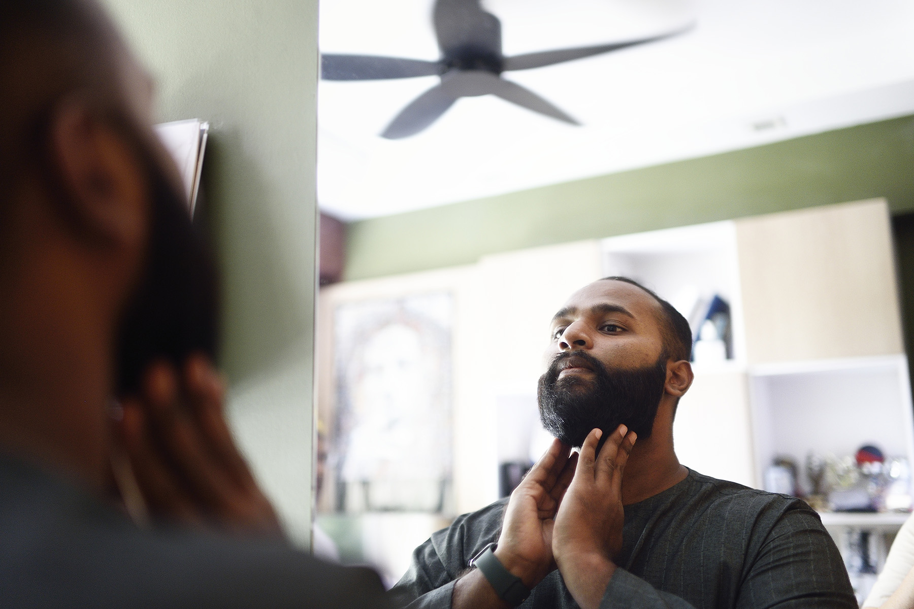 Man grooming his beard while looking in the mirror.
