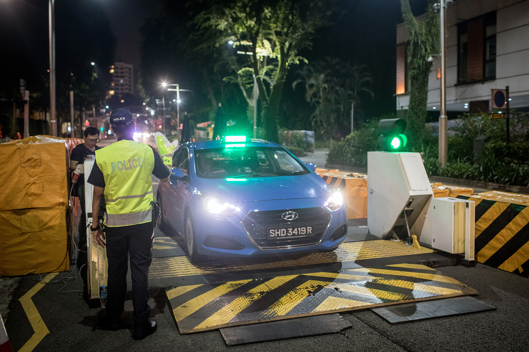 A police officer checks vehicles before they pass through a checkpoint. It is night.