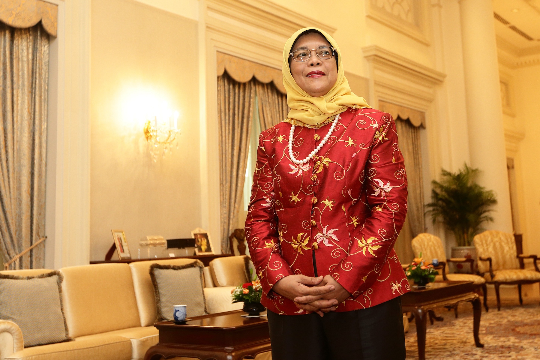 Singaporean President Halimah Yacob stands waiting for a diplomatic meeting with her hands folded and wearing a yellow hijab