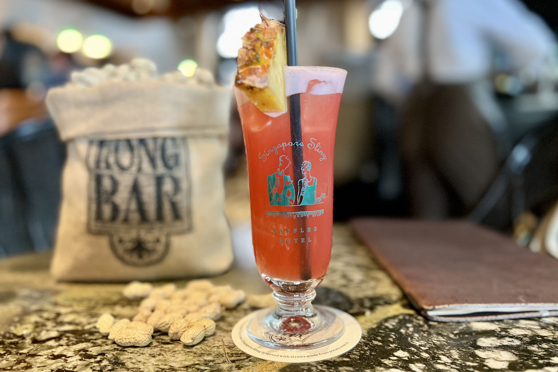 A classic pink Singapore Sling on a bar, served with peanuts, as is tradition.