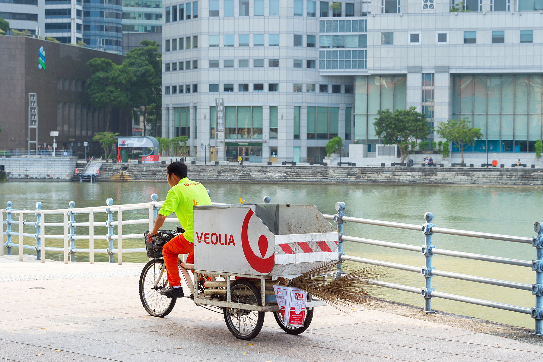 Garbage service worker cycling with his trash cart on a downtown embankment in Singapore.
