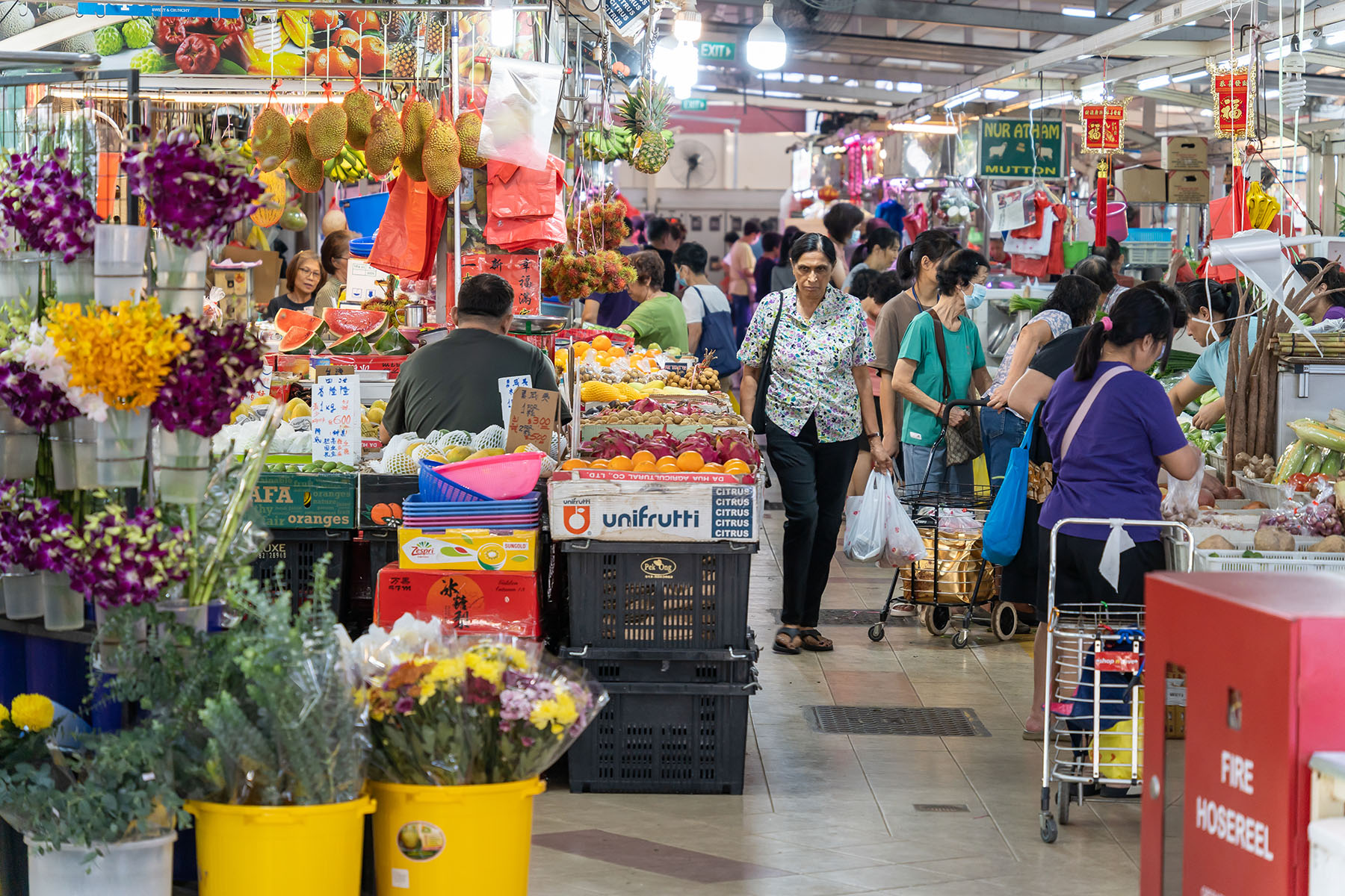 People walking at a wet market, buying flowers, fruits, and vegetables.
