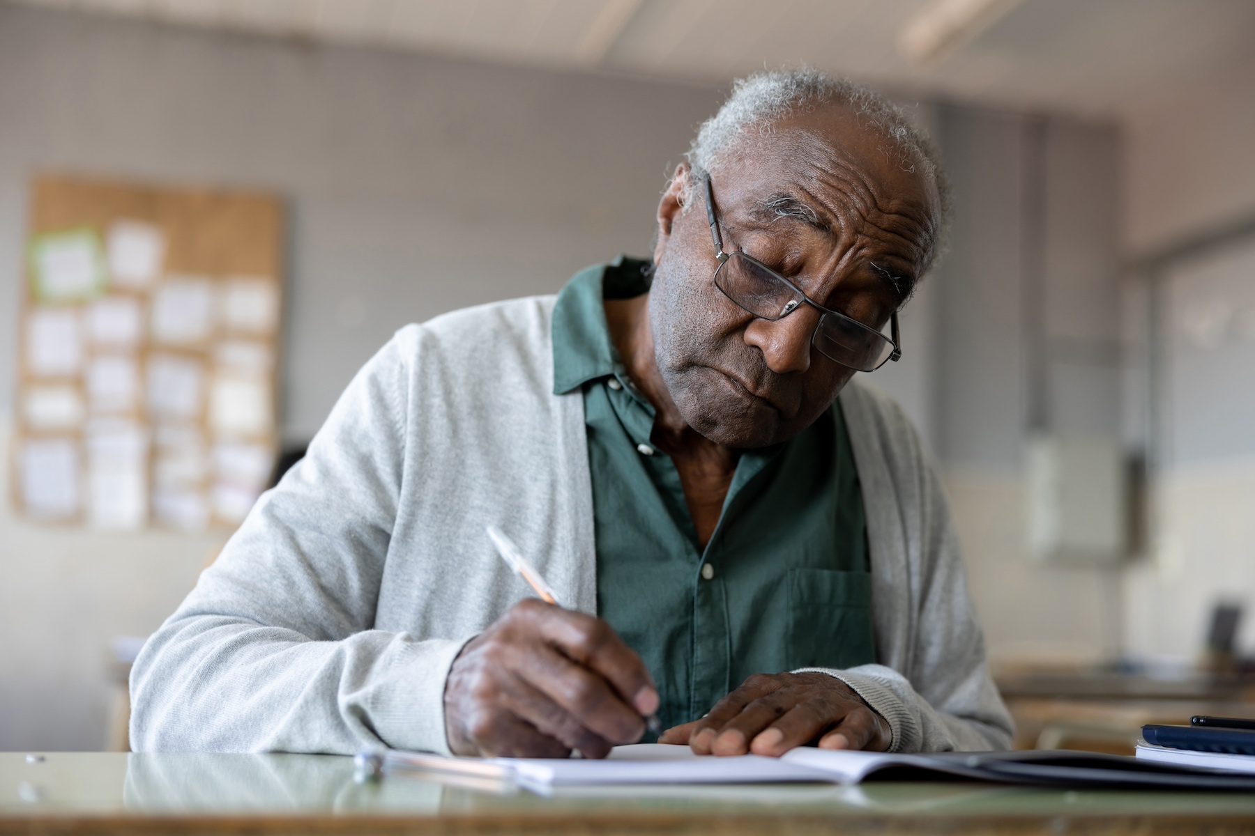 An older man takes a written language test in a classroom with pencil and paper
