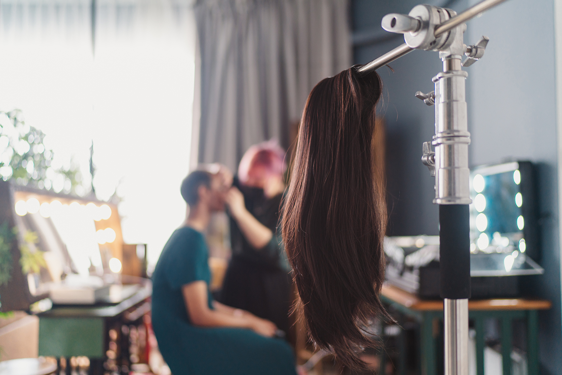 Out of focus picture of a trans woman getting ready, a wig hangs in the foreground