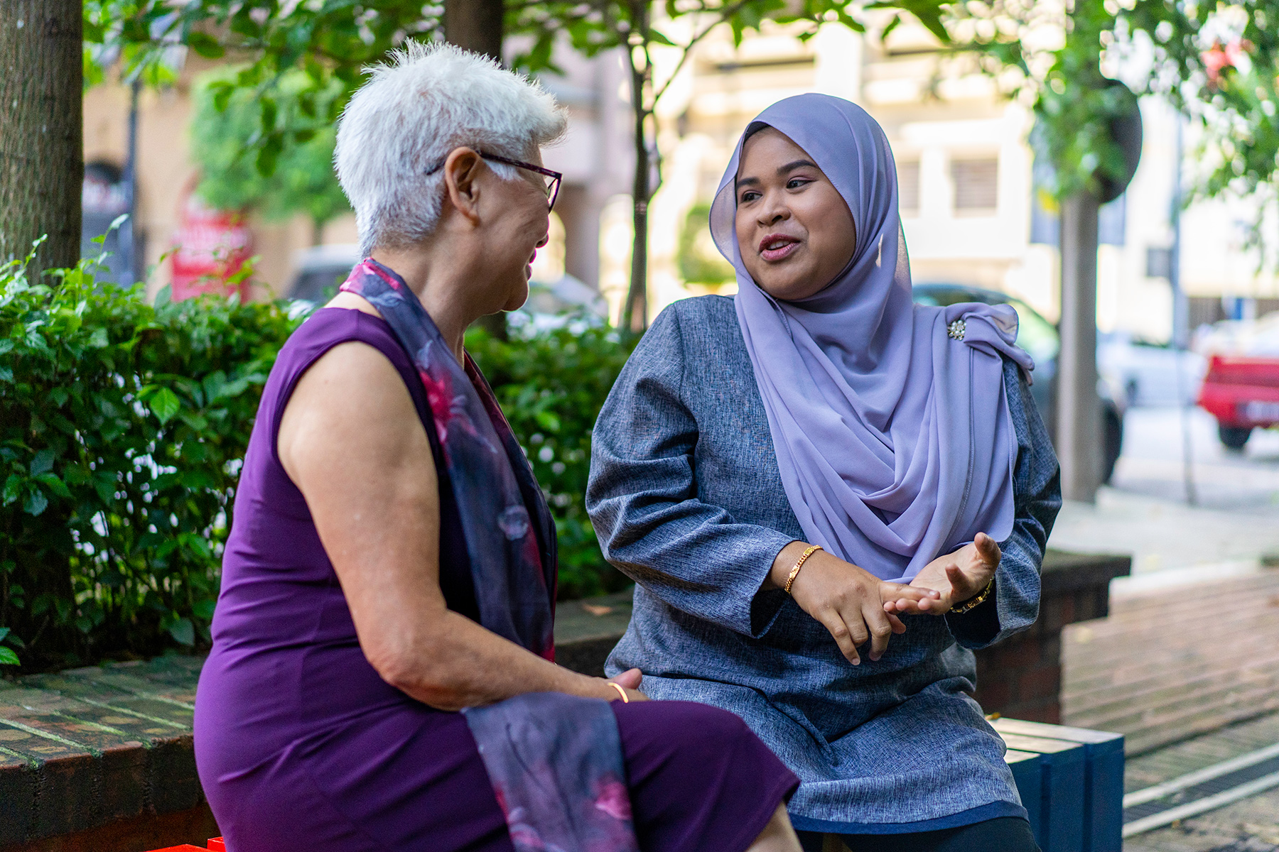 Two women chatting on a bench. One wearing a headscarf