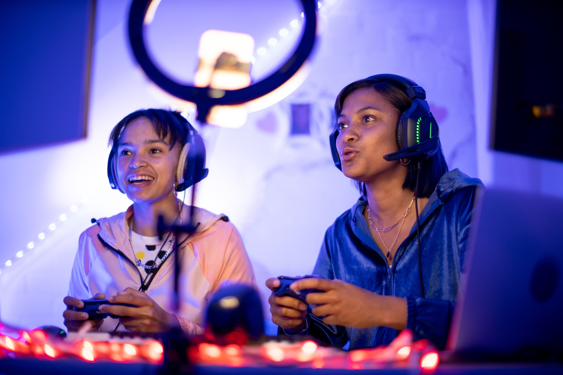 Two sisters play a video game together, each holding a controller and wearing a headset