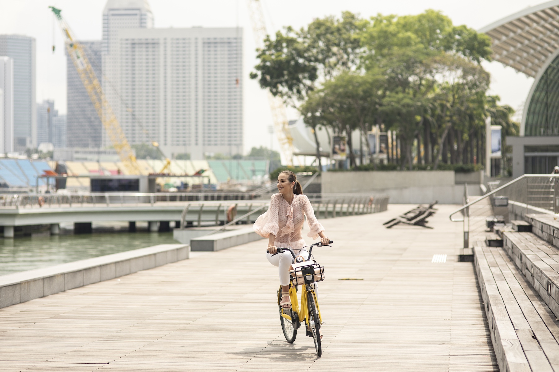 A woman rides a bike along the pier next to the water in Singapore on a bright sunny day