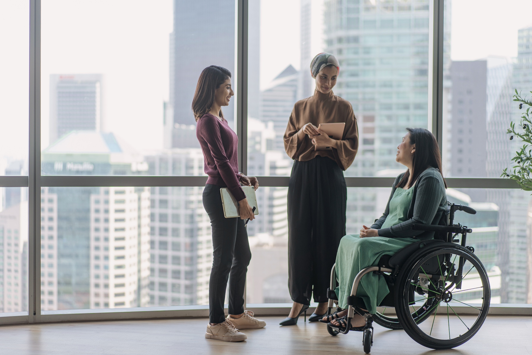 Three women discuss work matters near a window overlooking the Singapore skyline