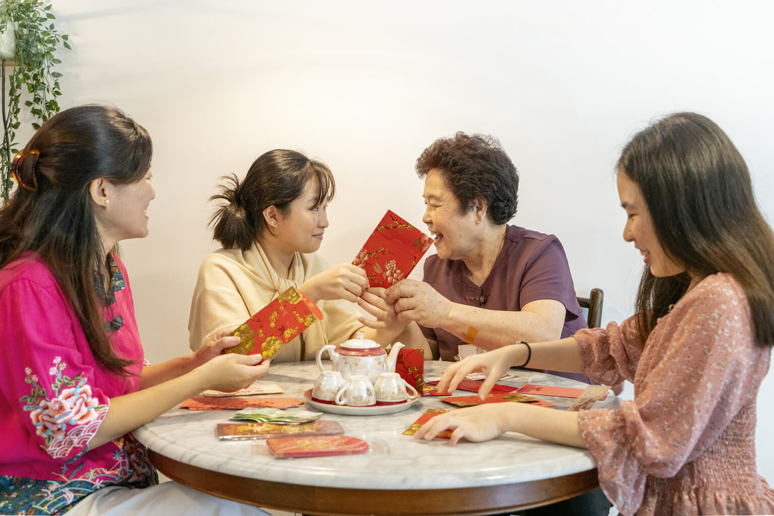Four women - possibly same family - sit around a table and chat -preparing for Chinese New Year by making red packets