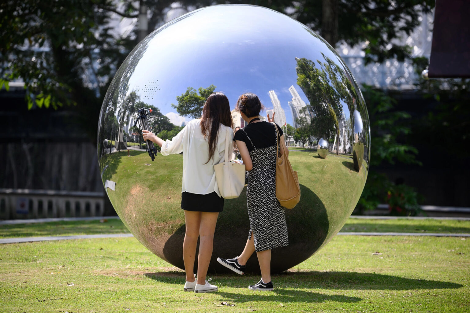 Two women looking at their reflections in a large metal ball