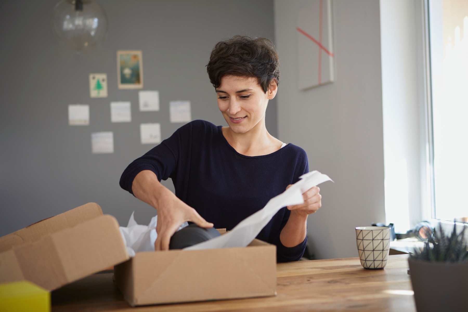 Smiling woman wrapping a package in a brown cardboard box and white paper