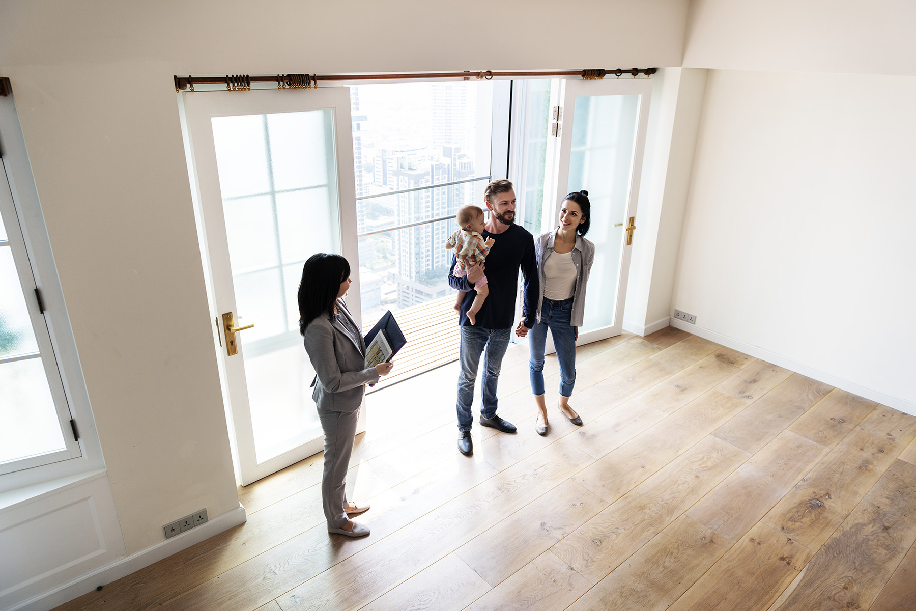 Young family looking at an empty flat, while a smiling realtor is standing close by.
