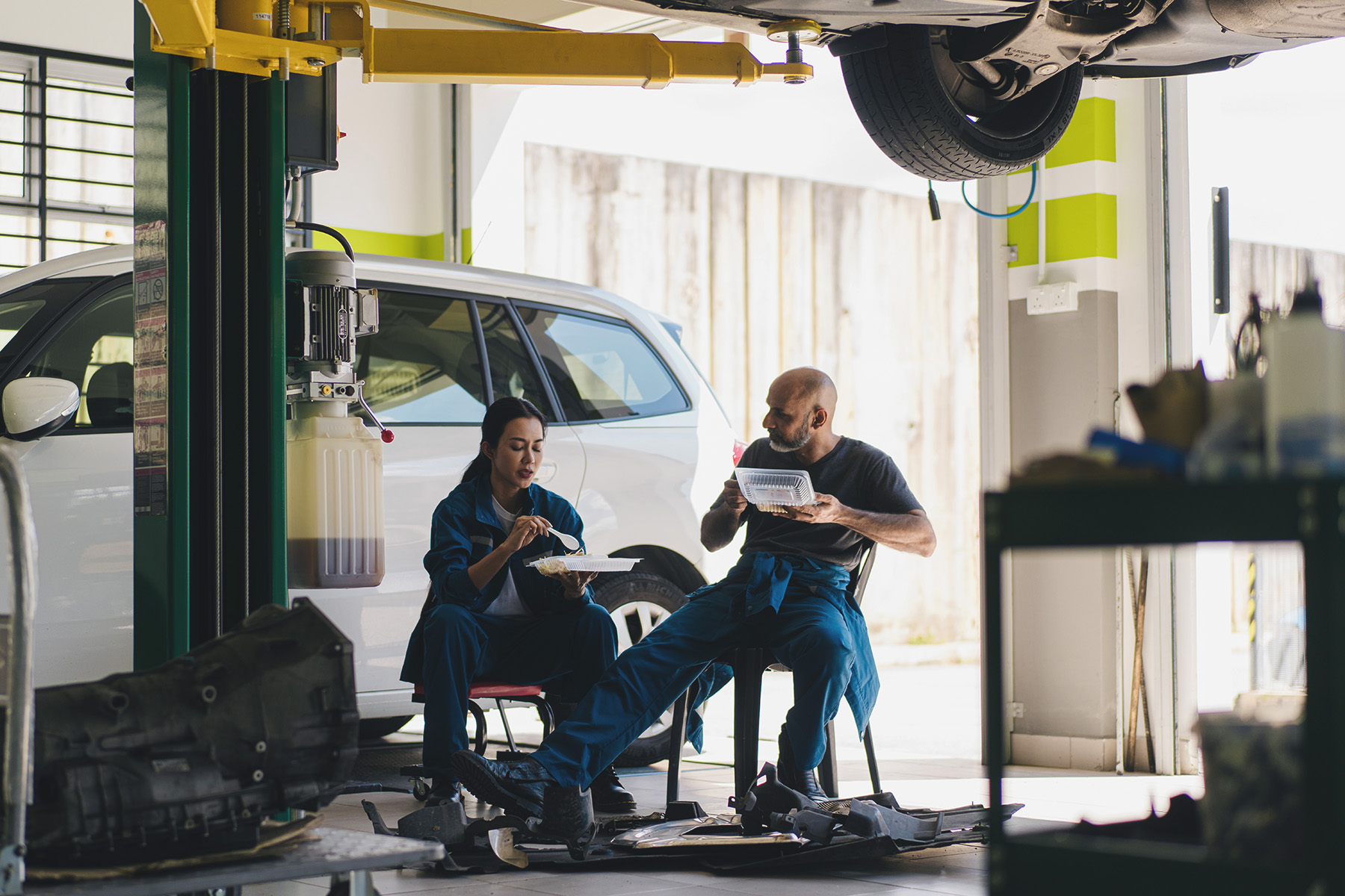 Senior mechanic and a young coworker talking during their a lunch break in the middle of the auto repair shop.