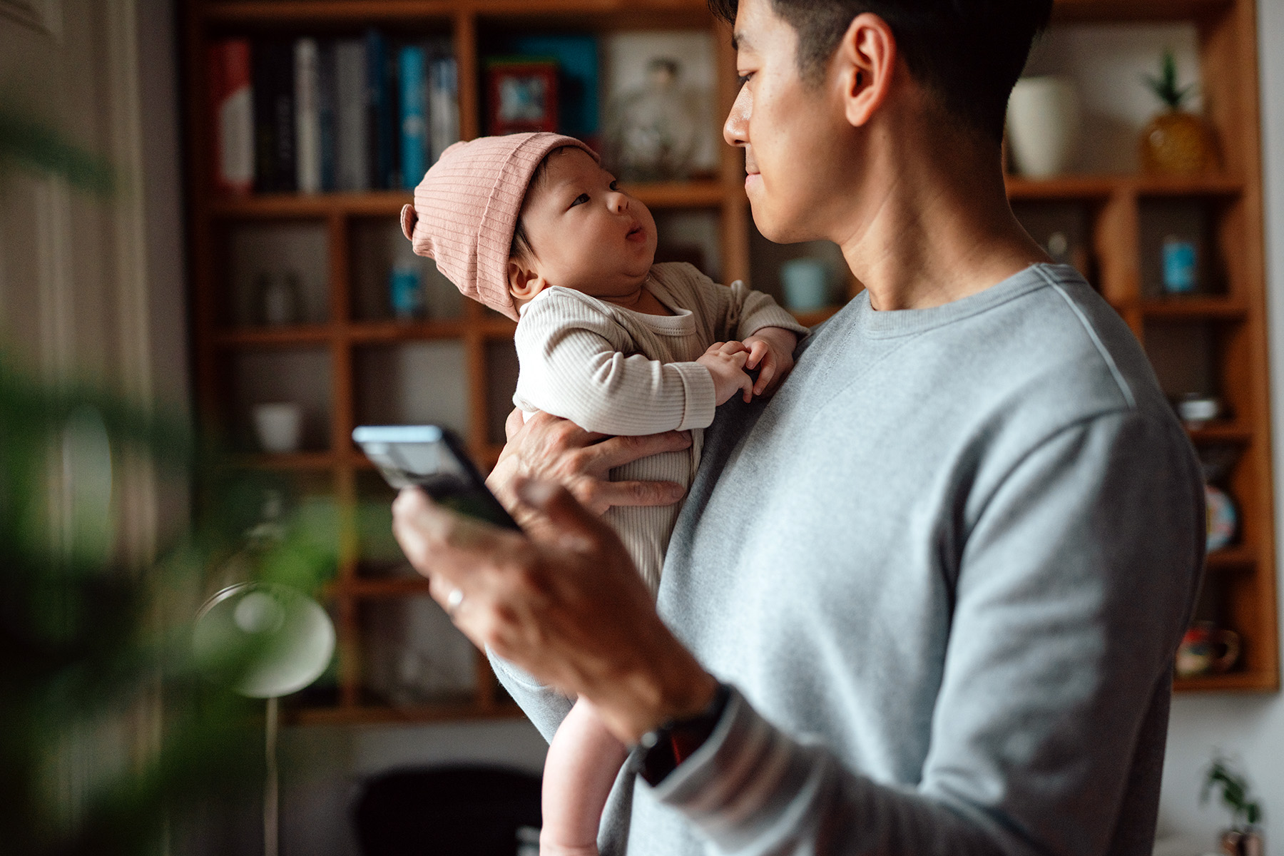 Father making faces at his baby who he is holding in his arms, while in one hand holding a smartphone.