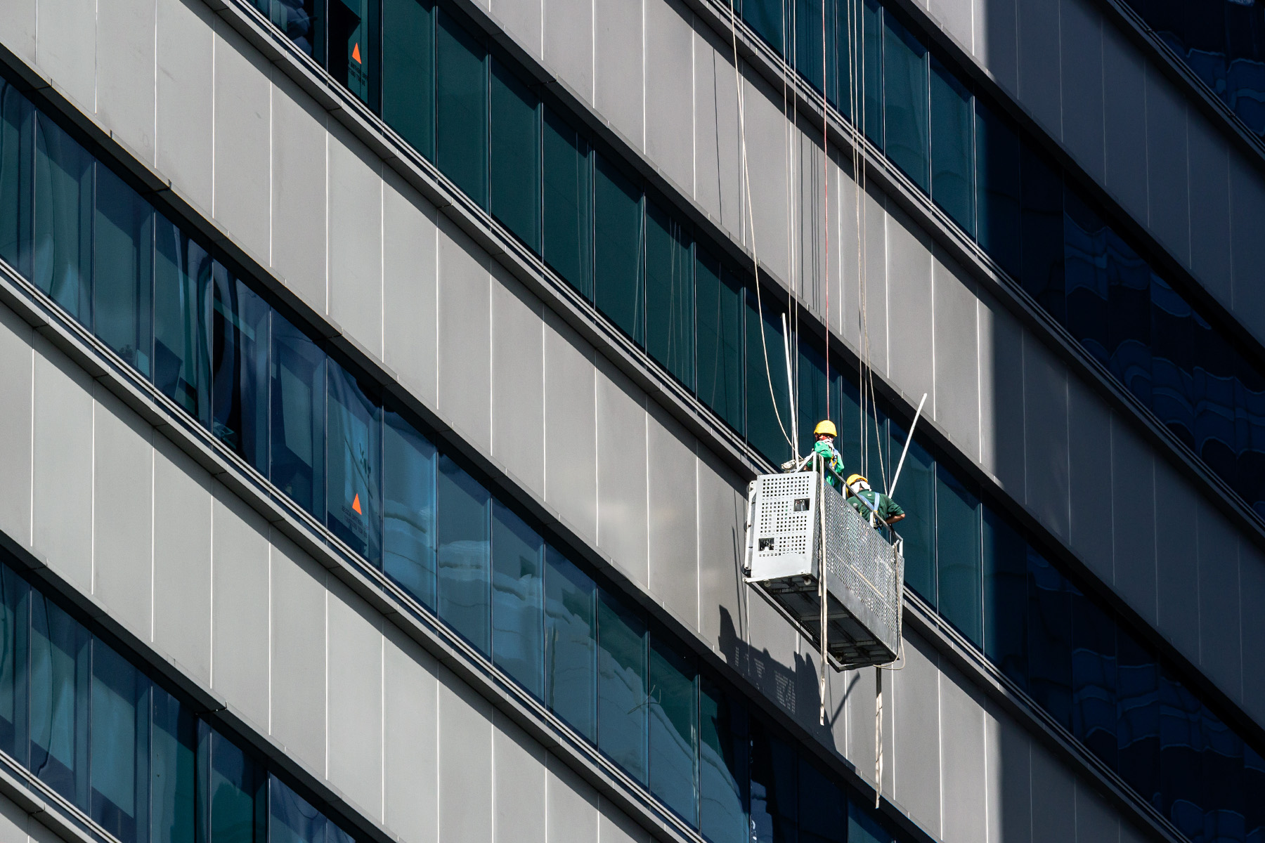 Two cleaners with hardhats and safety gear cleaning the windows of a skyscraper in Singapore.