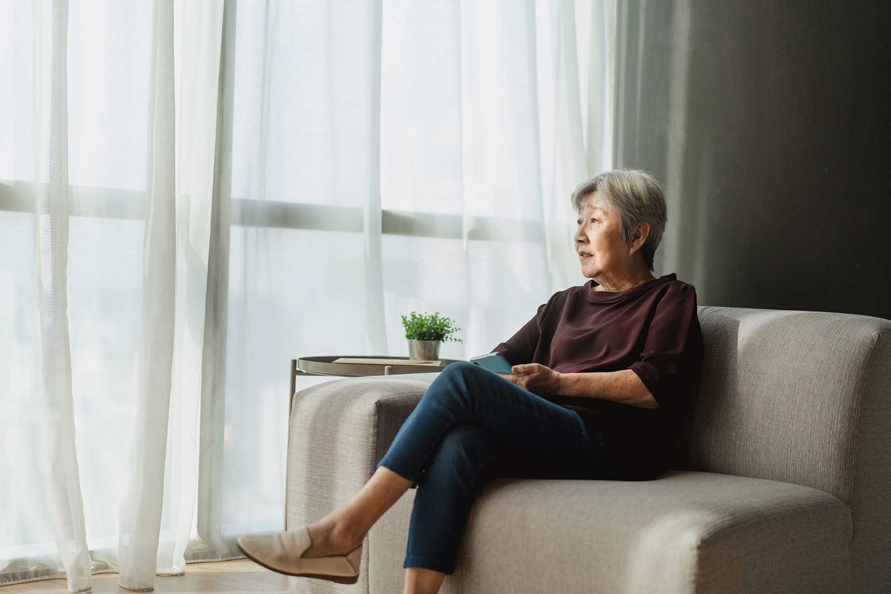 Older woman sitting in her couch looking out her window