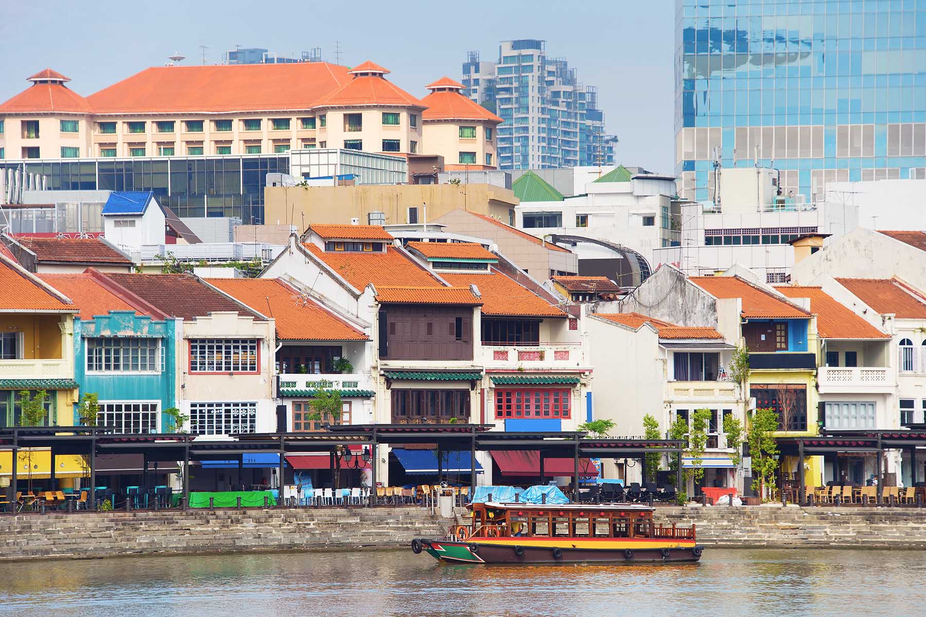 Poorly maintained houses in Boat Quay, the historial part of Singapore. The houses are built near the river and a boat is going by.