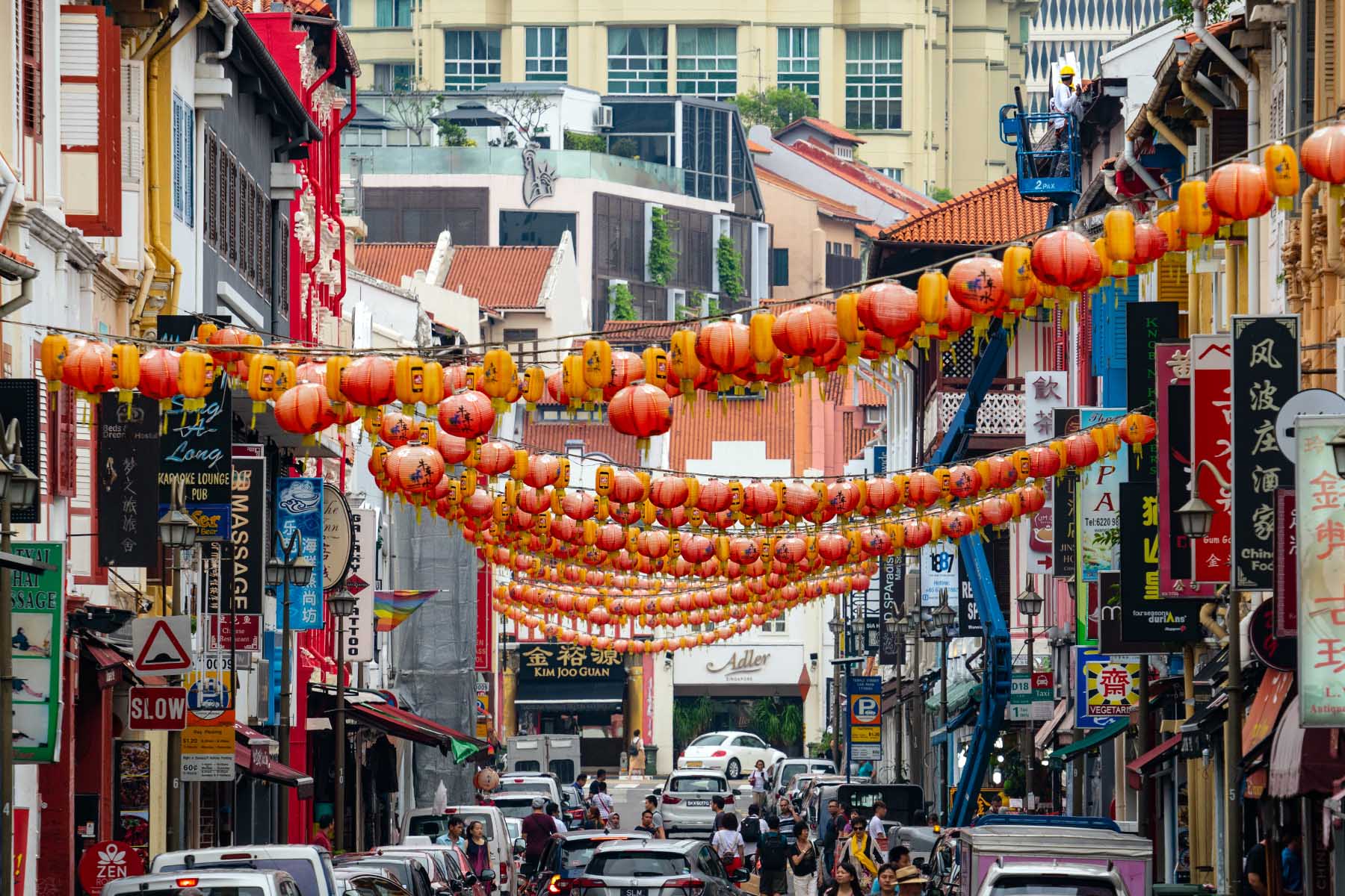 Bright red lanterns are hanging in the streets of Chinatown in Singapore. There's busy traffic.