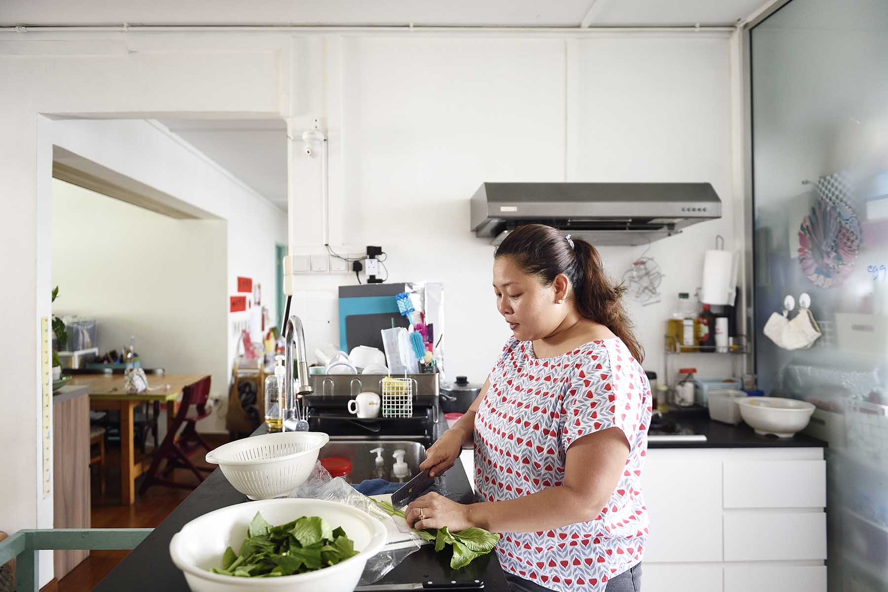 Woman standing in the kitchen, cutting vegetables. The house is messy.