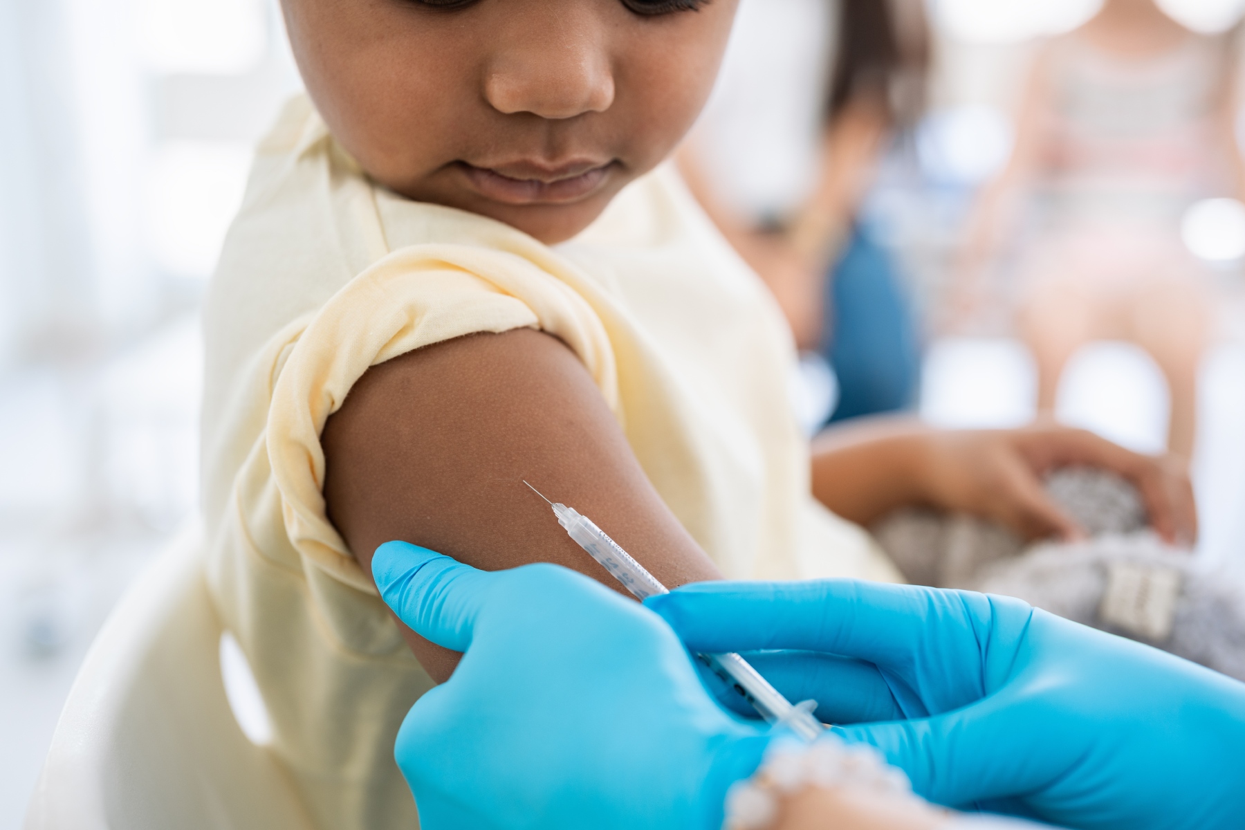a close-up shot of a Thai child receiving a vaccine from a healthcare worker who wears blue latex gloves