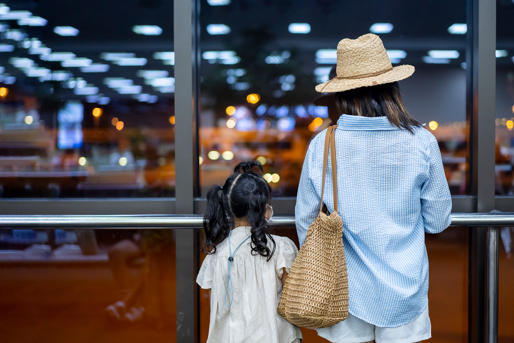 A parent and a child standing at a window in an airport, looking in.